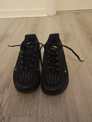 Svarta Nike Air Max Plus sneakers - Säljer ett par svarta Nike Air Max Plus sneakers med reflekterande detaljer och synlig Air-sula. Skorna har snörning, diskret vit swoosh och coola mönster på ovandelen. Perfekta för dig som gillar streetwear och sportig stil.
