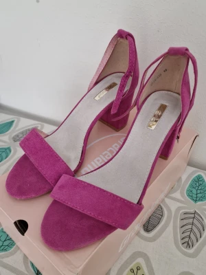 Rosa sandaler med klack från Graceland - Snygga rosa sandaler från Graceland med bred rem över tårna och justerbar rem runt ankeln. Klackarna är blockformade och ger både höjd och stabilitet. Materialet är mockaimitation som känns mjukt och trendigt. Perfekta för dig som vill sticka ut lite extra. Använda en gång, perfekt skick. Köpt i butik utomlands, inte på Shein-Temu.