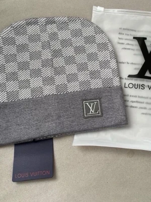 Grå mössa med rutmönster - Snygg grå mössa med klassiskt rutmönster och logga framtill. Mössan har vikt kant och är tillverkad i mjukt material som känns lyxigt. Perfekt accessoar för dig som gillar exklusiv stil. Endast mössa ingår