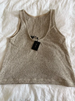 Beige stickad linnetopp Massimo Dutti - Säljer en beige stickad linnetopp med djup rundringning. Toppen har en mjuk, melerad struktur och är ärmlös med en avslappnad passform. Stl M/L.