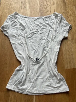 Vit topp med djup rygg - Säljer en vit topp från Ginatricot med korta ärmar och djup, öppen rygg. Mjukt material, lite tjockare tyg.