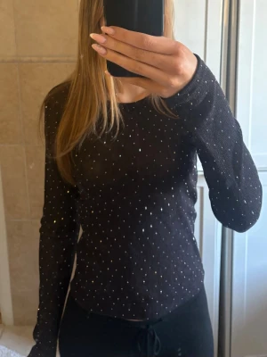 Svart glittrig långärmad topp - Snygg svart långärmad topp med glittriga detaljer som ger ett extra lyft till outfiten. Toppen har en tight passform och är tillverkad i ett tunt, stretchigt material som sitter skönt på kroppen. Perfekt för dig som vill sticka ut lite extra. Aldrig använd endast testad💕