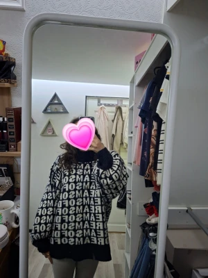 Svartvit stickad tröja med textmönster - Säljer en oversized svart stickad tröja med vit text i blockbokstäver över hela plagget. Tröjan har långa ärmar, breda muddar och en avslappnad passform. Perfekt för dig som gillar streetwear och statement-plagg. Storlek M men väldigt stor modell.