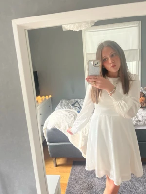 Vit omlottklänning med snörning - Säljer en vit kortklänning med långa ärmar och snygg snörning i ryggen. Klänningen har omlottdesign och markerad midja som ger en fin siluett. Perfekt för konfirmation eller skolavslutning💕