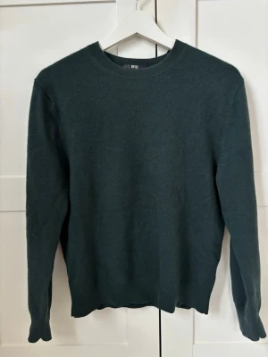 Mörkgrön stickad tröja Uniqlo - 100% kashmir, mörkgrön stickad tröja från Uniqlo med rund halsringning och långa ärmar. Tröjan har en enkel, stilren design och är tillverkad i mjukt material som passar perfekt till lager på lager. Ribbstickade muddar vid ärmslut och nederkant.