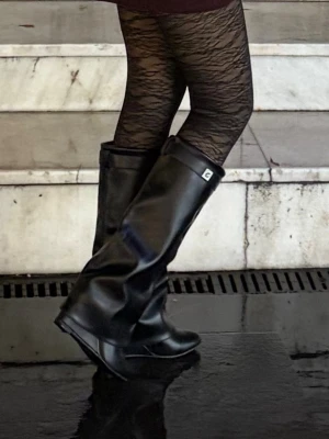 Svarta höga stövlar från Ganni - Säljer ett par svarta höga stövlar från Ganni i glansigt konstläder. Stövlarna har en bred skaftdesign, rund tå och en liten kilklack. Dekorativt spänne upptill och diskret logga på sidan. Perfekta för att lyfta din outfit med en edgy touch.