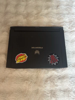 Acer Predator gaminglaptop svart - Säljer en svart Acer Predator gaminglaptop med cool design och två stickers på locket. Laptopen har en robust känsla och är byggd i plast och metall. Perfekt för gaming eller tunga program tack vare Predator-seriens prestanda.