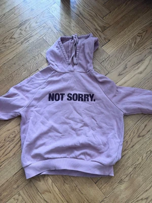 Ljusrosa hoodie från Gina Tricot - Ljusrosa hoodie från Gina Tricot med trycket 'NOT SORRY.' på bröstet. Mjuk insida, huva med dragsko och ribbade muddar. Perfekt för en avslappnad och trendig look.