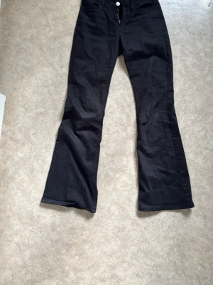 Svarta utsvängda jeans från Lindex - Svarta jeans från Lindex med utsvängda ben och klassisk femficksmodell. Jeansen har dragkedja och knapp framtill samt hällor för skärp. Perfekta för dig som gillar en retroinspirerad look.
