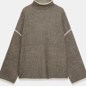 Brun stickad tröja med polokrage - Mysig brun stickad tröja med lös passform och polokrage. Tröjan har breda ärmar och vita kontrastsömmar vid hals, ärmar och axlar. Perfekt för lager på lager och en avslappnad stil