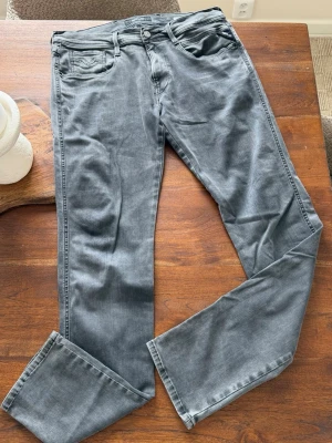 Grå jeans från Replay - Säljer ett par snygga grå jeans från Replay, modell Anbass. Jeansen har klassisk femficksdesign, raka ben och knappgylf. Materialet är mjukt och stretchigt för extra komfort. Perfekta för dig som vill ha en stilren och modern look.