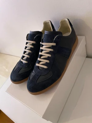 Maison margiela gats - Snygga mörkblå sneakers med ovandel i mocka och läder, vita snören och klassisk gummisula. Skorna har en stilren design med låg profil och passar perfekt till streetwear eller casual outfits.