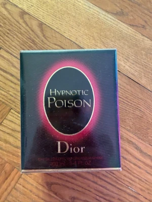 Dior Hypnotic Poison parfym 100ml - Dior Hypnotic Poison är en ikonisk parfym i en elegant svart och röd kartong med metalliska detaljer. Flaskan rymmer 100 ml och doften är känd för sin djupa, sensuella och mystiska karaktär. Perfekt för dig som gillar lyxiga och unika dofter.