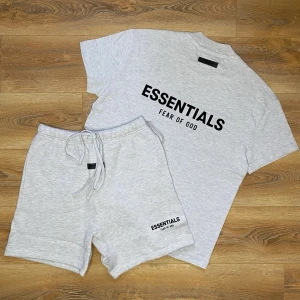 Essentials grått set från Fear of God - Säljer ett stilrent grått set från Essentials by Fear of God. Setet består av en t-shirt och shorts i mjukt material med svart logga tryckt på både tröjan och shortsen. Perfekt för en avslappnad och trendig look.