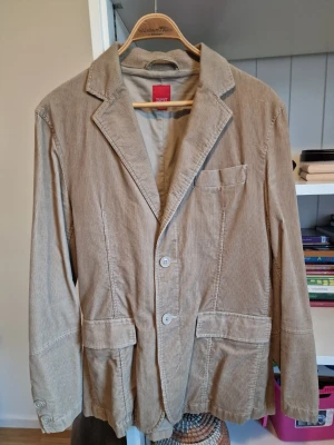 Beige manchesterkavaj från Esprit - Snygg beige kavaj i manchestertyg från Esprit. Klassisk modell med tre knappar framtill, tre fickor och breda slag. Perfekt för dig som vill ha en avslappnad men ändå stilren look. Passar till både jeans och chinos.