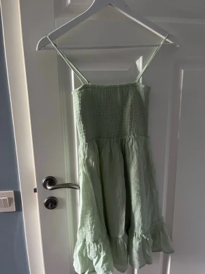 Ljusgrön sommarklänning med volang - Söt ljusgrön klänning med smala axelband och volang nertill. Klänningen har smockad överdel och är tillverkad i ett lätt material som passar perfekt för varma dagar. Den har en luftig och avslappnad passform.