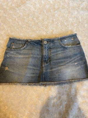 Blå jeanskjol med slitna detaljer - Jätte snygg jeanskjol i blå denim med slitna detaljer och rå kant nertill! Storlek S, midjemått på bilden. Använd 1 gång. Skriv frågor eller prisförslag💘