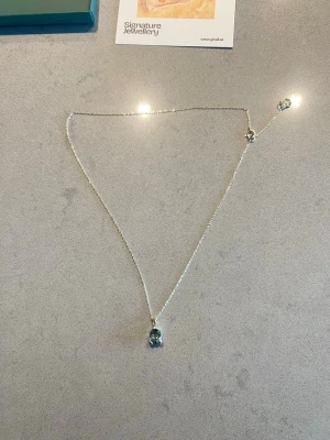 Silverhalsband med grön sten från Ylva Li - Ett elegant halsband i silver från Ylva Li med en tunn kedja och ett hängsmycke med en rektangulär blå sten. Perfekt för att ge din outfit en stilren touch. Levereras i originalask.