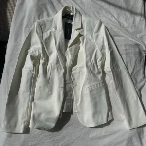 Vit kavaj från Vero Moda - Stilren vit kavaj från Vero Moda med klassisk krage, två fickor framtill och enkelknäppning. Perfekt för en clean och fräsch look. Materialet är slätt och ger en snygg siluett. Perfekt till studenten! Pris kan diskuteras!