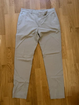 Beige kostymbyxor från Zara - Snygga beige kostymbyxor från Zara med klassisk rak passform och bälteshällor. Byxorna har diskret knapp- och dragkedjestängning samt är tillverkade i ett mjukt och bekvämt material. Perfekta för en stilren och avslappnad look.