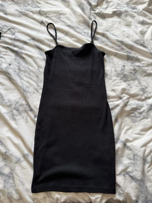 Svart ribbad klänning från Amisu - Säljer en svart ribbad klänning från Amisu i storlek 36. Klänningen har smala axelband och ärmlös design med en kroppsnära passform. Perfekt för dig som gillar enkel och stilren look.