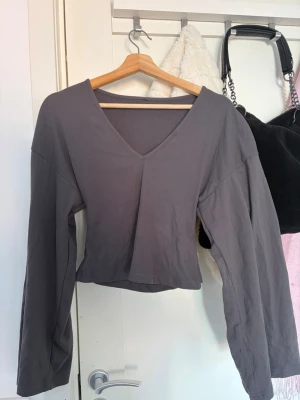 Grå långärmad v-ringad topp - En stilren grå långärmad topp med v-ringning och rak passform. Toppen är enkel och passar perfekt till jeans eller kjol. Tillverkad i mjukt material som känns skönt mot huden.