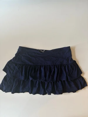 Mörkblå kjol - Supersöt mörkblå kortkjol med dubbla volanger och bred resår i midjan. Perfekt för dig som gillar en lekfull och trendig stil. Kjolen är lätt och passar till många olika outfits.