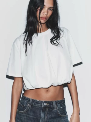 Vit croppad topp med ballongfåll - Trendigt croppad vit topp med ballongfåll och rund hals. Toppen har korta ärmar och en loose passform som ger en avslappnad vibe. Perfekt att styla med höga jeans eller kjol för en cool look.