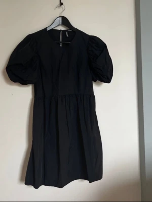 Svart kort puffärmad klänning H&M - Svart klänning från H&M med kort längd och puffiga korta ärmar. Klänningen har rund halsringning och en enkel, stilren design som passar perfekt till många tillfällen.