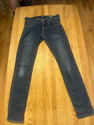 Mörkblå replay anbass jeans - Snygga mörkblå slim fit jeans från replay med klassiska fem fickor och diskreta slitningar på benen. Jeansen har normal midja och raka ben, tillverkade i stretchigt denim för en bekväm passform. Perfekta för en trendig och avslappnad stil.