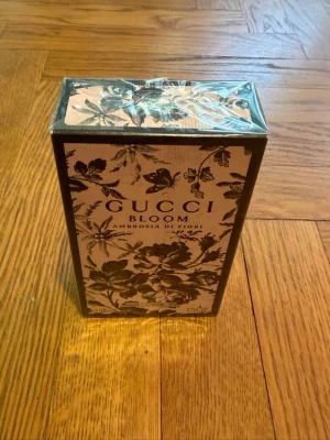 Gucci Bloom Ambrosia di Fiori parfym - Gucci Bloom Ambrosia di Fiori är en lyxig parfym i en snygg rektangulär kartong med blommigt svart mönster på ljusrosa botten. Förpackningen har tydlig Gucci-logga och elegant design som känns exklusiv och trendig. Perfekt för dig som gillar unika och blommiga dofter.