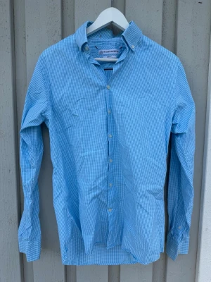 Blå rutig skjorta från The Shirt Factory - Säljer en blå och vit rutig skjorta från The Shirt Factory med slim fit-passning. Mycket bra skick - Storlek 39 ungefär M
