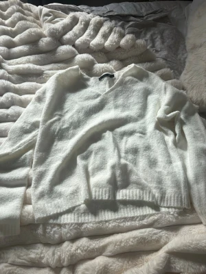 Vit stickad tröja med v-ringning - Mysig vit stickad tröja med v-ringad hals och långa ärmar. Tröjan har ribbade muddar vid ärmslut och nederkant. Perfekt för lager på lager och enkel att matcha med olika outfits.