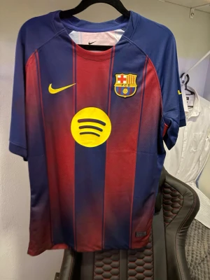 FC Barcelona matchtröja Nike - Säljer en FC Barcelona matchtröja från Nike med klassiska blå och röda ränder, klubbmärke och Nike-logga på bröstet samt Spotify som sponsor. På ryggen står det Lamine Yamal och nummer 10 i gult. Perfekt för dig som älskar fotboll och Barca.