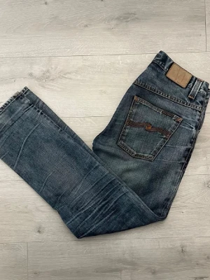 Blåa nudie jeans - Säljer ett par blåa jeans från Nudie Jeans i regular fit. Jeansen har tydlig användning/fade vilket ger en riktigt snygg och naturlig vintage-look.  • Färg: Blå denim med slitningar och fading • Fit: Regular fit • Skick: Använda med karaktär • Sitter skönt och får en clean relaxed stil • Perfekta till både sneakers, hoodie och stickat • Äkta denimkänsla med snyggt worn-in utseende