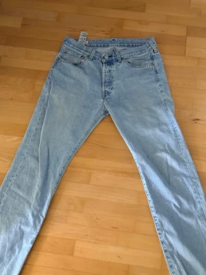 Levi's ljusblå raka jeans 501 - Säljer ett par klassiska ljusblå jeans från Levi's med rak passform och fem fickor. Jeansen har gylf med knappstängning och är tillverkade i bomull. Perfekta för en avslappnad och tidlös stil.