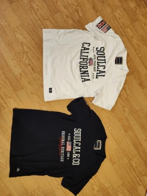 SoulCal t-shirts med tryck - Två t-shirts från SoulCal&Co, en vit och en marinblå, båda med tryck framtill. Bra skick men den vita har en liten blå fläck, se bilder. Herr stl S på båda.