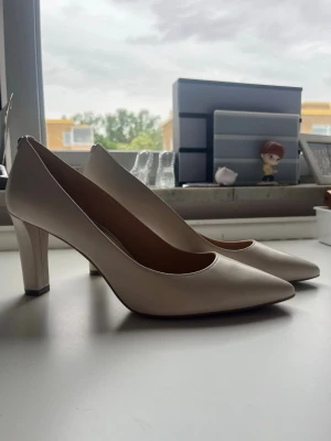 Snygga vita klackar från Michael Kors 🍾 - Säljer ett par stilrena pumps i vit färg med spetsig tå och hög klack från Michael Kors. Skorna har en elegant och tidlös design, perfekta för att lyfta din outfit. Materialet är slätt och ger ett exklusivt intryck. Passar dig som gillar klassiska och snygga skor. Perfekta för studenten eller bröllopet 🍾🥂