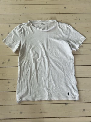 Vit t-shirt från Polo Ralph Lauren - Klassisk vit t-shirt från Polo Ralph Lauren med broderad marinblå logga nertill. T-shirten har rund halsringning och korta ärmar. Perfekt basplagg i mjuk bomull som funkar till allt.
