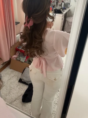 Ljusrosa omlottopp med knyt - Supersöt ljusrosa omlottopp med v-ringning och knyt i ryggen. Toppen har korta, vida ärmar och markerad midja som ger en feminin siluett. Perfekt för dig som gillar romantisk och trendig stil.