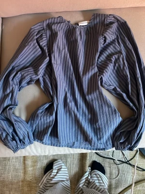 Blårandig blus från Carin Wester - Snygg blus från Carin Wester i blått med tunna vita och svarta vertikala ränder. Blusen har rund halsringning och långa ärmar med resår vid ärmsluten. Tillverkad i ett lätt, glansigt material som ger en stilren look.