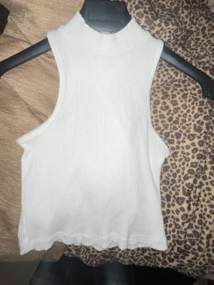 Vit ribbad ärmlös topp Lager 157 - Säljer en vit ribbad ärmlös topp från Lager 157 med hög hals. Toppen är croppad och har stretchigt material som sitter snyggt på kroppen. Perfekt att styla med jeans eller kjol för en trendig look.
