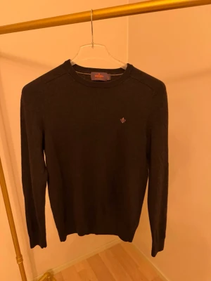 Mörkbrun stickad tröja Morris - Snygg mörkbrun stickad tröja från Morris med rund halsringning och diskret logga broderad på bröstet. Tröjan har långa ärmar och ribbade muddar vid ärmslut och nederkant. Perfekt till höst och vinter för en stilren look. Orginala priset 1599kr 