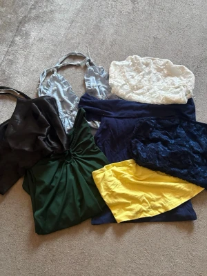 Klädpaket sommar  - Paket med sommartoppar  i olika färger och material. Innehåller bland annat ett ljusblått halterneck-nattlinne i satin, grön långärmad topp och svart linne samt bandeau-toppar i vitt spets, blå spets och gul bomull. Perfekt för dig som gillar variation på sommaren