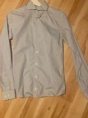 Blå super slim skjorta från Eton - Snygg ljusblå skjorta från Eton i super slim passform. Skjortan har klassisk krage, vita knappar och långa ärmar. Perfekt för dig som gillar en stilren och modern look. och skjortan har diskreta ränder. Köpte för över 1500