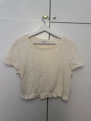 Ribbad croppad topp från NA-KD - Säljer en ljus, ribbad croppad topp från NA-KD. Toppen har korta ärmar, rund halsringning och elastisk nederkant. Perfekt till jeans eller kjol för en avslappnad look.