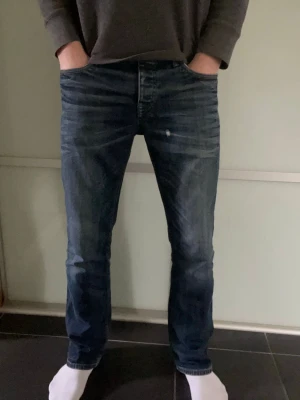 Blå raka jeans från jack&jones - Säljer ett par klassiska blå jeans från jack&jones med rak passform och snygg slitning. Jeansen har fem fickor, knappgylf och detaljer i kopparfärg. Materialet är kraftig denim. Perfekta för en avslappnad och trendig look. Finns mindre slitning på framsida lår samt mindre färg stänk som syns på biler. Storlek 32:32 jag är 183cm och de passar perfekt.