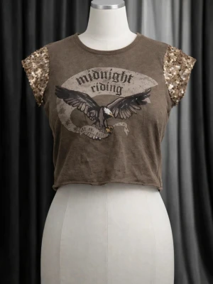 Brun croppad topp med paljetter - Snygg brun croppad topp med texten 'midnight riding' och en stor örn på bröstet. Ärmarna är korta och täckta med glittriga paljetter som ger en cool kontrast. Perfekt för dig som vill sticka ut lite extra.