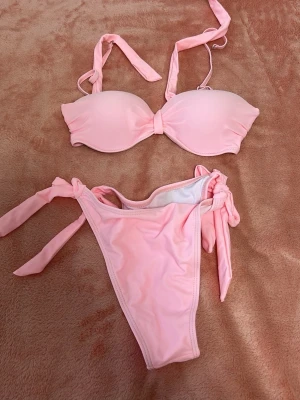 Ljusrosa bikini med knyt - Söt ljusrosa bikini med vadderad bandeau-topp och knyt i nacken samt på sidorna av bikinitrosorna.  Aldrig använd eller testad, köpte fel färg