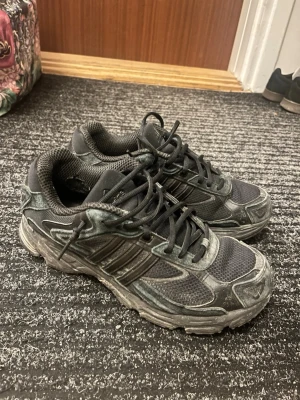 Svarta Adidas sneakers med mesh och läder - Säljer ett par svarta Adidas sneakers med klassiska tre ränder på sidan. Skorna har en kombination av mesh och läderdetaljer, samt en robust sula. Perfekta för dig som gillar sportig och street-inspirerad stil.